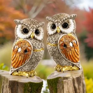 Pair of decorative owl statues with intricate feather detailing, golden accents, and reflective embellishments placed on a wooden surface.