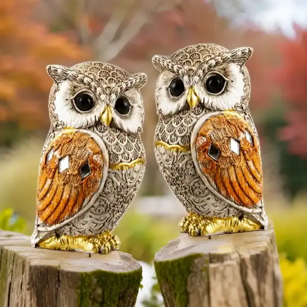 Pair of decorative owl statues with intricate feather detailing, golden accents, and reflective embellishments placed on a wooden surface.